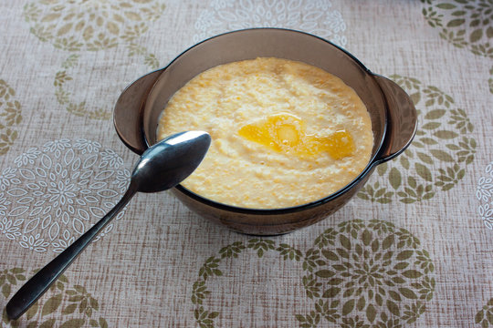 Tasty millet porridge with butter and milk in a glass plate with a metal tablespoon