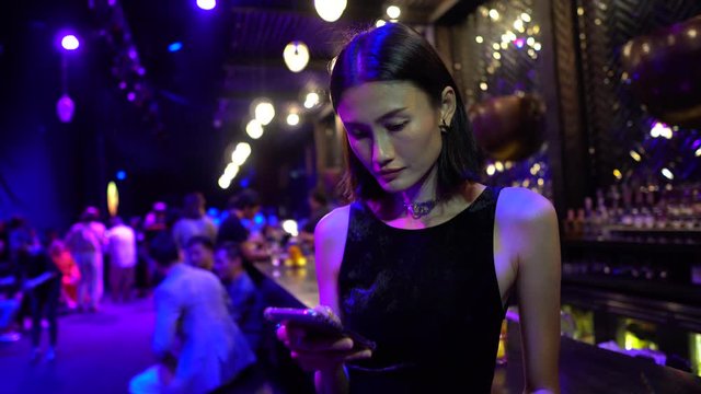 An Asian woman at a bar checks messages on her smartphone