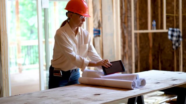 Woman architect reviewing blueprints with computer tablet in a new home construction project inspection.