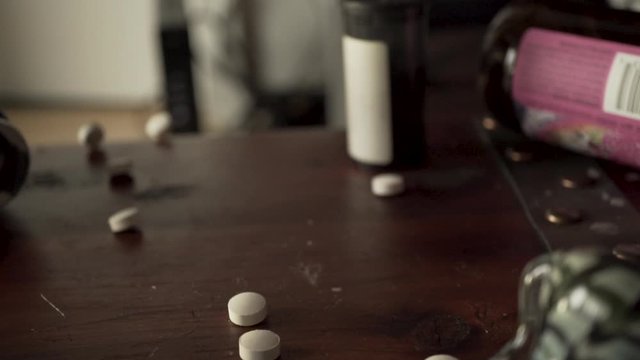 Slow motion falling painkiller pills on table with beer, addiction concept