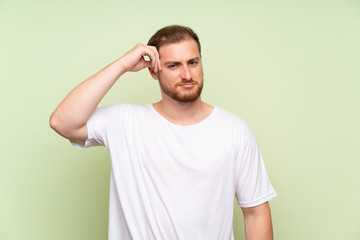 Handsome man over green background having doubts and with confuse face expression