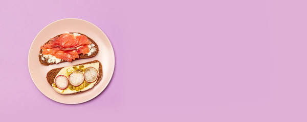Fresh sandwich with red fish, feta cheese cucumber and pesto on a pink ceramic plate on a purple background