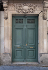 Classical architecture columns and stone relief decorations above wooden framed door painted in green color with brass handles. Rectangle shape entrance of retro building in Paris France.