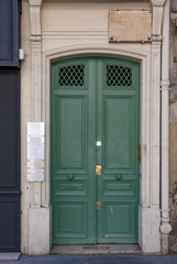 Old wooden door. Classical architecture door painted in matte green color with round doorknobs and golden keyhole plate. Framed entrance of old stone building in Paris France.