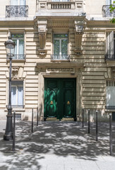 Old house. Facade of building of classical architecture style. White windows and front door painted in green color. Elegant entrance of retro house in Paris France. Shadows from foliage on sidewalk.