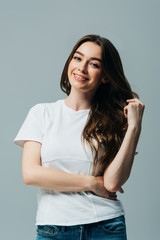 Obraz premium happy beautiful girl in white t-shirt touching hair isolated on grey