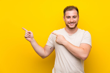 Handsome man over yellow background pointing finger to the side