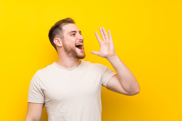 Handsome man over yellow background shouting with mouth wide open