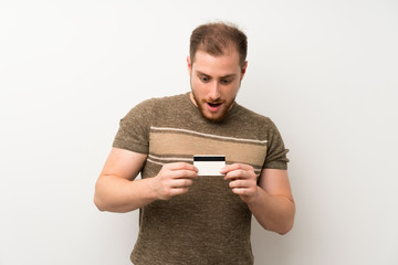 Handsome man over isolated white wall holding a credit card