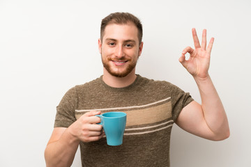 Handsome man over isolated white wall holding hot cup of coffee