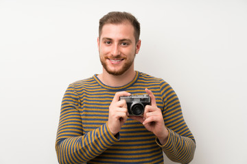 Handsome man over isolated white wall holding a camera