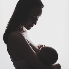 Authentic silhouette of a young woman with a newborn baby in her arms breastfeeding