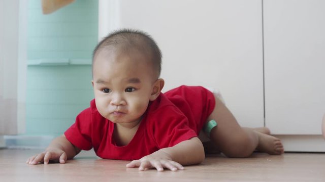 Cute baby boy wearing red shirts are lying and playing on the wooden floor.