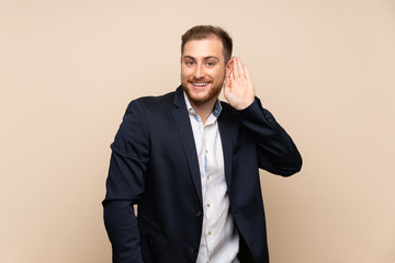 Blonde man over isolated background listening to something by putting hand on the ear