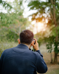Rear view of a professional male photographer holding vintage film camera to take photo in the evening sunset