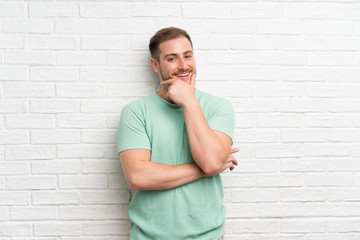 Blonde man over brick wall laughing