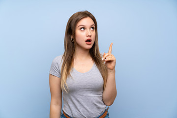 Teenager girl over isolated blue wall thinking an idea pointing the finger up
