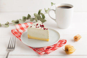 Piece of cheesecake on gray plate on kitchen spatula and cup of coffee on background