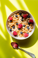 Healthy breakfast with berries,dried fruits, nuts, cereals top view copy space.cornflakes with raspberries and blueberries on yellow background.Sweet cornflakes with berries and milk as healthy meal