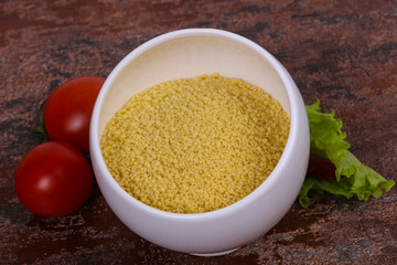 Raw couscous in the bowl served salad leaves, tomato and pepper