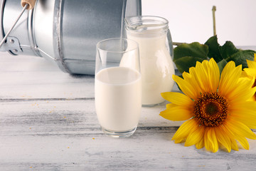A jug of milk and glass of milk on a wooden table and flower