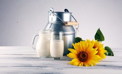 A jug of milk and glass of milk on a wooden table and flower