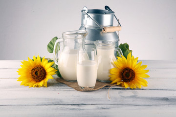 A jug of milk and glass of milk on a wooden table and flower