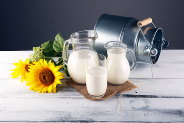 A jug of milk and glass of milk on a wooden table and flower