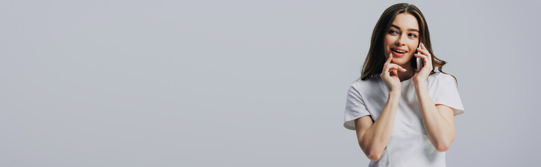 cunning beautiful girl in white t-shirt talking on smartphone isolated on grey, panoramic shot