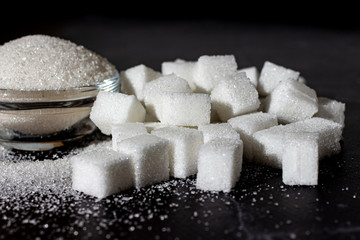 Sugar on a black background. Sugar wave. Sugar and pieces of sugar are poured.