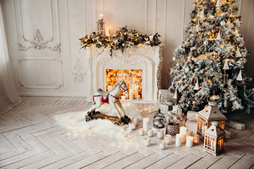 classical luxury interior of a white room with Christmas tree with garland, decorated fireplace, rocking horse, gifts for new year