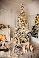 classical luxury interior of a white room with Christmas tree with garland, decorated fireplace, rocking horse, gifts for new year