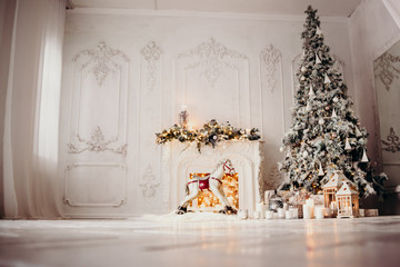 classical luxury interior of a white room with Christmas tree with garland, decorated fireplace, rocking horse, gifts for new year