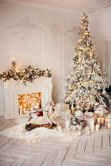 classical luxury interior of a white room with Christmas tree with garland, decorated fireplace, rocking horse, gifts for new year