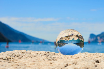 Obraz premium Lake Garda (Lago di Garda or Lago Benaco) seen through a glass crystal ball placed on rock. Selective focus