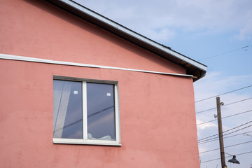 Light red top of a house with a window and sloping roof on a background of blue sky