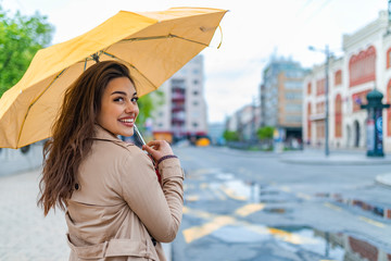 Attractive young woman standing at bus station and waiting a bus. Business, weather and people...