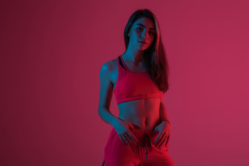 Young fitness woman posing in sportswear against red light background.