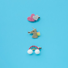 Set of children's shiny hair clips in the form of a unicorn, rainbow and hearts on a blue background.