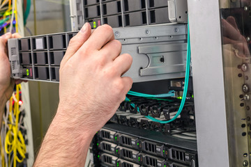 Installation of a new server in a rack with computer equipment is close up. System administrator's hands hold a powerful supercomputer. Performing work to replace server in the data center
