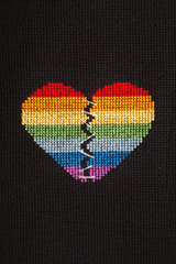 Broken heart embroidered on black cloth with rainbow threads. Heart sewn with white threads.