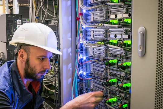  A specialist connects the wires in the server room of the data center. A man works with telecommunications. The technician switches the Internet cable of the powerful routers