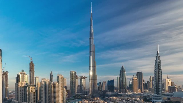Dubai Downtown skyline timelapse with Burj Khalifa and other towers with long shadows during sunrise paniramic view from the top in Dubai, United Arab Emirates. Traffic on circle road and old style