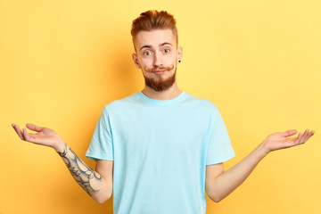 serious young handsome man with funny moustache looking at camera and spreading hands. Isolated on yellow background.It's a piece of cake