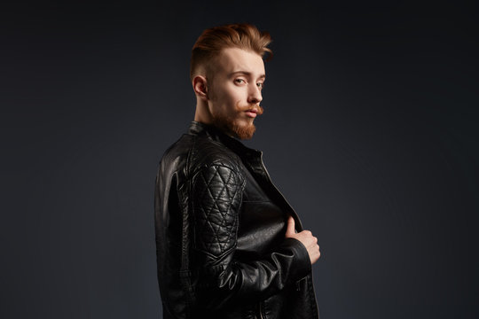 stylish young man taking off his leather jacket. isolated black background, studio shot. autumn, fall season clothes.