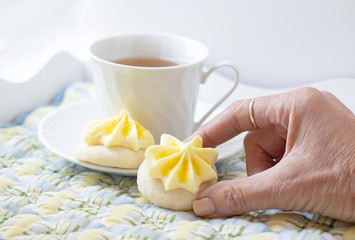 Original photograph of a woman's hand holding a home made lemon frosted cookies with a cup of tea on white