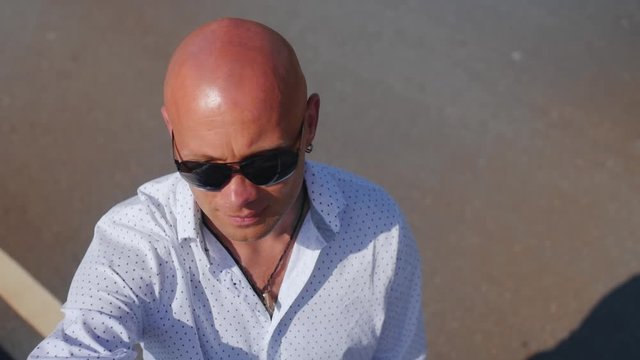 Portrait of a bald man in sunglasses looking up. Close up shot.