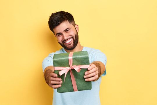 Cheerful Positive Kind Man Giving A Present To A Friend, Isolated Yellow Background, Studio Shot. Kindness, Positive Feeling And Emotion. It's For You. Love, Friendship Concept