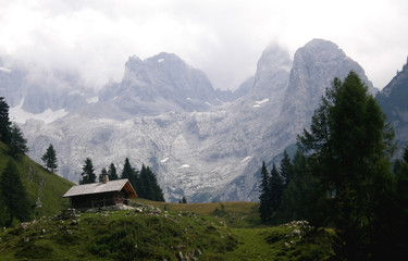 Mała chata wysoko w górach pośród alpejskich szczytów - obrazy, fototapety, plakaty