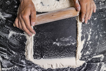 Female hands with rolling pin with flour on dark table. Baking background. Flour, cooking and baking concept. Copy space, top view
